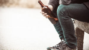 Den liberala synen på alkohol kan kännas främmande för dem som kommer längre ifrån. Man sitter på en bänk med en flaska i handen.