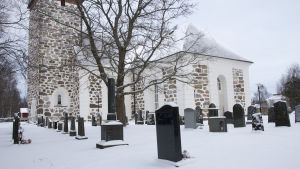 Någonstans här gräver man upp två lik för att se om de dött en naturlig död eller inte. En stor vit stenkyrka. Framför kyrkan finns flera gravstenar. Det är vinter och snö på marken.