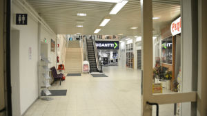 En bild från insidan av ett köpcentrum. På bilden syns en rulltrappa och två affärer.