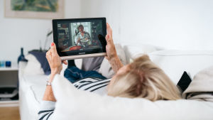 Kuvassa mummo makaa sohvalla ja katsoo ohjelmaa tabletilla