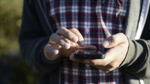 En person håller en smarttelefon i handen och håller fingret ovanpå skärmen.