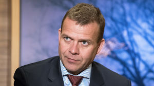 Petteri Orpo, Samlingspartiet:"Vi fortsätter satsa på förebyggande åtgärder. Kommunerna måste göra upp planer för hur de främjar barn och ungas välmående och för hur de ordnar och utvecklar barnskyddet. Regeringens spetsprojekt satsar på en reform av den här servicen och vi har beviljat pengar till projekt runtom i Finland. I landskapen har det utsetts förändringsagenter, som ska främja spetsprojektets målsättningar i landskapen.” Petteri Orpo i mörk kostym. I bakgrunden en suddig tavla.