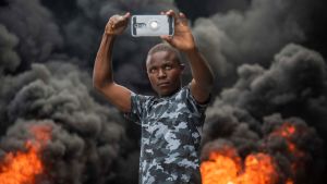 En demonstrant tog en selfie mot bakgrunden av brinnande bildäck i Port-au-Prince på söndagen. En demonstrant tog en selfie mot bakgrunden av brinnande bildäck i Port-au-Prince på söndagen.
