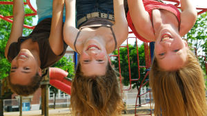 tre långhåriga flickor hänger skrattande upp och ner i en klätterställning