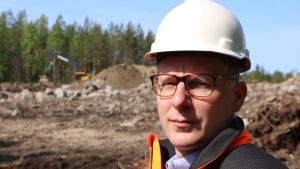 Hans Vadbäck. En man med glasögon och vit hjälm på huvudet står vid ett markarbete. I bakgrunden skymtar en grävmaskin.