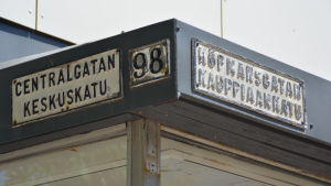 En bild på tre slitna gatuskyltar på en vägg. På en står det centralgatan en annan nummer 98 och en tredje köpmansgatan