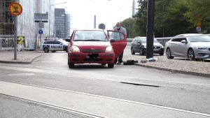 Polisen samlar in bevismaterial från brottsplatsen. En röd bil som står tillbucklad mitt på Sandviksgatan, och en polis som undersöker den.