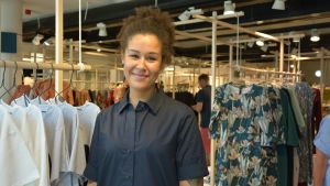 Effi Bangura har inte märkt av att kunderna skulle minska på grund av oljudet. En ung leende, tjej står framför olika kläder som hänger i butiken.