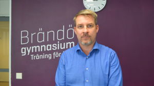 Brändörektorn Mikael Nyholm är bekymrad över hur skolans utrymmen räcker till i och med distanskraven. En man i blå skjorta som står framför en lila vägg tittar mot kameran.