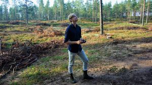 Kartograf Aleksi Rikkinen sköter kartläggningen av området i samband med grävningarna. Ung man står och håller en fjärrkontroll för en drönare i skogen.