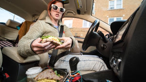 Nainen autossa ajajan paikalla kädet voileivässä kiinni.