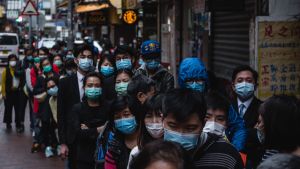 Hongkongbor köar för att få ansiktsmasker. En lång kö med människor med ansiktsmask på en gata i en stad.
