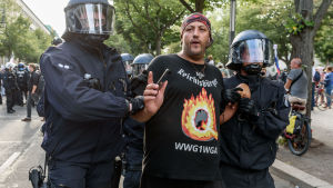 Konspirationsteorin har också spridit sig till Tyskland där Q-anhängare deltagit i demonstrationerna mot coronarestriktioner Två kravallpoliser leder bort en man.