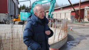 Seppo Knuuttila är forskare vid Finlands miljöcentral. Man med blå dunjacka står framför tank med gödsel på bondgård.