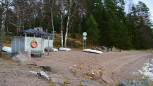 Omklädningsrummen vid lägergården står öde och tomma. Sandstrand. Roddbåtar ligger upp och ner. Små omklädningsrum.