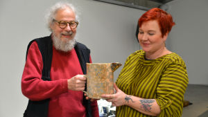 Pia Hynninen och Kai Nieminen håller i en av Elina Sorainens kannor. Pia Hynninen och Kai Nieminen med Elina Sorainens kanna i händerna.