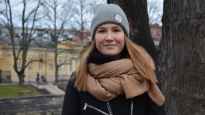 Ida Bengtfolks tycker att man borde handla med eftertanke. Ida Bengtfolks, en ung kvinna med långt hår iklädd grå mössa och svart rock ser in mot kameran i ett grått Åbo vid aura Å.
