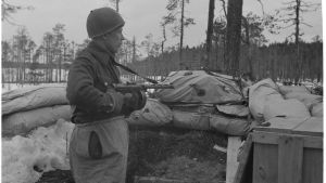 Det är viktigt för många veteraner att få tala ut om sina erfarenheter. Bild från en skyttegrav i Rukajärvi. Fortsättningskriget, april 1943. En soldat står i en skyttegrav. Skog syns i bakgrunden.
