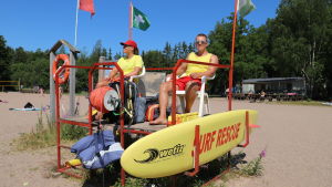 Badvakterna Emma Uusküla och Severi Lehtinen övervakar badgästerna på Ekvalla badstrand. Två badvakter på en simstrand.