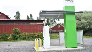 Den verkliga lönsamheten ligger inte i att producera energi för lantgårdens behov, det är i trafiken som pengarna bränns av. På bilden biogasstationen vid Knehtilän tila. Grönvit tankningsstation på en sandplan, lagårdsbyggnader i bakgrunden.