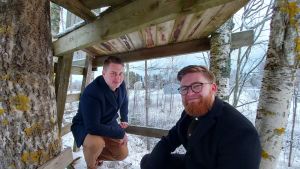 Joel Åman och Herman Nyqvist uppe i den träkoja som Åman byggde som liten. Att bygga var ett substitut till att se på tv kanske? I Kotkamaa syntes nämligen inte Svt.. Två män uppe i träkoja. Vintriga fält i bakgrunden.