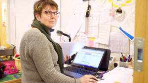 Mervi Harvio-Jokiaho sitter vid ett skrivbord och jobbar med några papper och en dator.