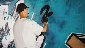 Janne arvostaa kaupungin antamaa mahdollisuutta graffititaiteilijoiden maalata betonipinnoille vanerilevyjen sijaan. Janne Saarikoski täydessä touhussa spraymaalaamassa seinää.