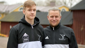 Rufus och Rafael Kesti. Rufus Kesti och Rafael Kesti står brevid varandra framför en röd träbyggnad.