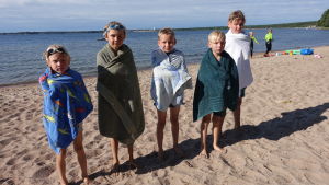 Ludvig, Benjamin, Emil, Filip och Anton har just kommit upp ur vattnet efter det första simpasset. Simskoledeltagarna Ludvig, Benjamin, Emil, Filip och Anton står på stranden med handdukar runt sig.