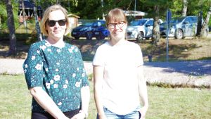 Från vänster Heli Boije, Sabina Mattinen (föräldrar till barn som deltar i simskolan i Karskog, Sjundeå) Två kvinnor står på ett soligt gräsplan. Bilar i bakgrunden. Sommar. De ler.