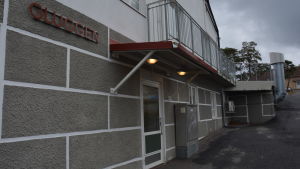 Gluggen finns nu i Stabshuset i Korpo kyrkby. Grå stenbyggnad fotad från sidan.