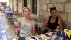 Ivana Šepak (till vänster) utanför den resebyrå hon driver i en gränd i Dubrovniks Gamla stad. Ivana Šepak sitter med en kollega vid ett cafébord i en gränd i Dubrovniks Gamla stad.