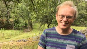 Peik Grönholm har ordnat kurser i landskapsvård och hållit i projekt där långtidsarbetslösa har aktiverats i landskapsvård. En bild på en man i t-skjorta och i bakgrunden syns ängsmark.