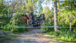 Polisen har spärrat av brandplatsen och tagit över undersökningen av brandorsaken. Eldhärjat hus i grönskande sommarmiljö