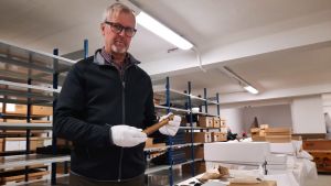 Guy Björklund visar upp en luntbehållare som användes för att tända kanoner. En man håller i en metallhylsa i en lagerlokal.