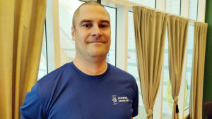 Benny Forsström har fått tummen upp av simhallsbesökare som uppskattar att simhallen har öppet igen. En man med rakat huvud och blå t-skjorta. I bakgrunden stora fönster där man kan se bassängerna i Ekenäs simhall.