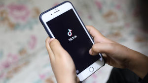 Att vara populär på TikTok kan vara en stor fördel ifall man är ute efter ett skivkontrakt. Scrolla längre ner för att läsa mer om vad det beror på. En person håller i en vit telefon. I skärmen syns Tiktoks logo; svart bakgrund med en not och texten "Tiktok".