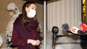 Statsminister Sanna Marin vill inte se att man lättar på restriktionerna i det här skedet. Sanna Marin med munskydd framför mikrofoner på Ständerhusets snöiga trappa.