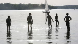 Ungdomar i vattnet och en segelbåt.