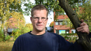 Thomas Hansson har delat ut post i Ingå skärgård i över tio år. Postutdelaren Thomas Hansson står vid ett äppelträd. I bakgrunden syns träd med gula löv.
