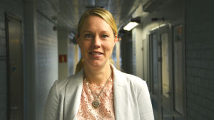 Johanna Bonäs är historielärare och läroboksförfattare. johanna bonäs står i en lång ganska mörk korridor. hon bär en vit blus och kavaj.