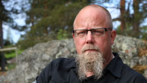 Tekniska direktören Ari-Johan Myllyniemi. En medelålders man med långt skägg och glasögon sitter på en bänk.