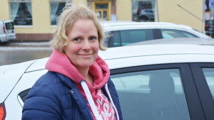 Arbetet som uppsökande ungdomsabetare sträcker sig över hela Sibbo och Weckström får således tillbringa en hel del tid i bilen. En blond kvinna står intill en vit bil i stadsmiljö.
