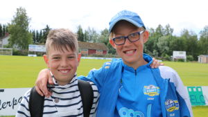 Adam Simons och Hannes Laine. Två pojkar håller om varandra vid en fotbollsplan.