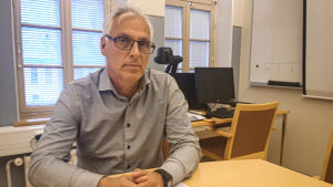 Jan Levander. Jan Levander sitter vid ett skrivbord och tittar in i kameran med allvarlig min.