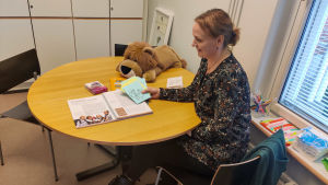 Enligt skolkurator Anne-Maj Kuoppamäki handlar det mycket om att stanna upp och diskutera med barnen för att stöda deras välmående. En kvinna som sitter vid ett runt träbord och håller upp kort.
