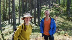 Egenlandin juontajat Hannamari Hoikkala ja Nicke Aldén seisovat metsäisellä harjulla, taustalla näkyy polku.