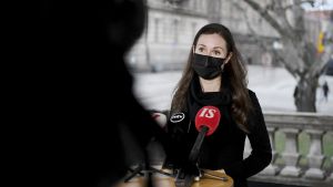 Sanna Marin (SDP) sa att alla måste ge efter om det är frågan om en kompromisslösning. Statsminister Sanna Marin (SDP) i svart munskydd vid Ständerhusets trappor. Hon talar i mikrofoner som ställts framför henne.