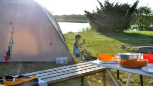 Lapsi lukee kirjaa teltan edessä.