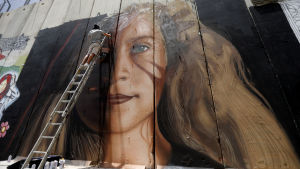 Väggmålning föreställande Ahed Tamimi, som blivit en uppskattad symbol för motståndet i Palestina. Vissa tror att hennes ljusa drag gör att konservativa israeler också tvingas erkänna hennes existens och att hon därför är ett samtalsämne i landet. Väggmålning föreställande Ahed Tamimi.